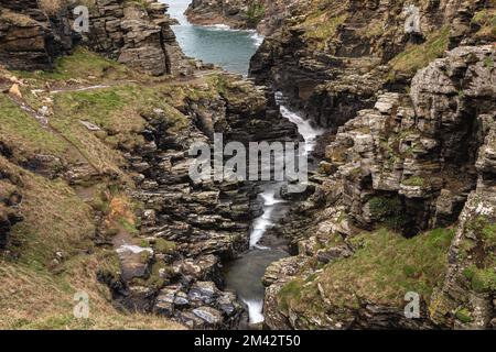 Ich schaue auf einen Fluss, der durch eine Schlucht fließt, und dann hinaus aufs Meer. Tintagel, Cornwall Stockfoto