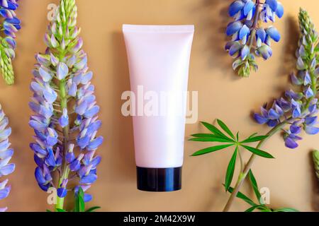 Rosafarbener Kosmetikschlauch mit schwarzem Schraubverschluss und Lupinenblumen auf goldgelbem Hintergrund. Creme Feuchtigkeitscreme Hautpflegeprodukt blank p Stockfoto