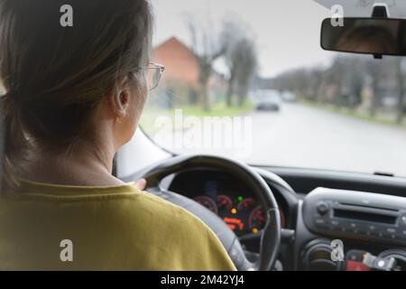 Frau am Steuer. Rückansicht einer Autofahrerin. Eine Brille. Aufmerksamkeit auf die Perspektive der Straße. Fahrschule Stockfoto