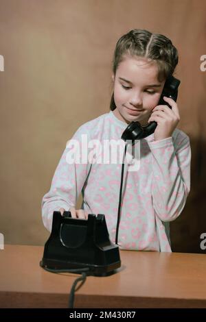 Retro-Porträt eines Mädchens mit Telefon. Das Teenager-Mädchen wählt eine Nummer auf einem alten Telefon. Stockfoto