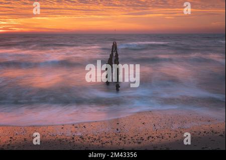 Sonnenaufgang über der Nordsee auf East Mersea Island in Essex. Wellenbrecher im Langzeit-Meer. Warmer, roter, orangefarbener und gelber Morgenhimmel. Lebendige Farben Stockfoto