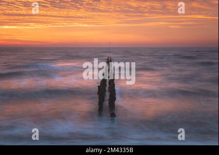 Sonnenaufgang über der Nordsee auf East Mersea Island in Essex. Wellenbrecher im Langzeit-Meer. Warmer, roter, orangefarbener und gelber Morgenhimmel. Lebendige Farben Stockfoto