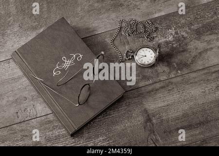 Zeit zum Schlafen. Altes Buch, Brille und Taschenuhr auf einem strukturierten Tisch. Altmodisches Stillleben Stockfoto