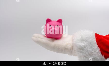 Die Hand des Weihnachtsmanns hält ein Sparschwein in seiner Hand Stockfoto