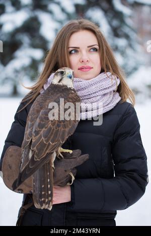 Ein Mädchen in einem schwarzen Mantel hält im Winter einen Falken an der Hand Stockfoto