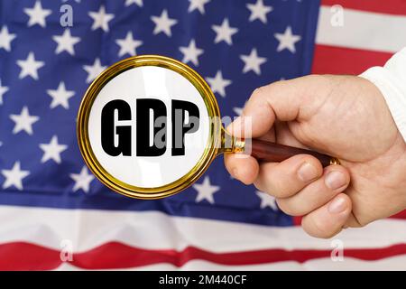 Vor der amerikanischen Flagge hält ein Mann eine Lupe in der Hand mit der Inschrift GDP. Stockfoto