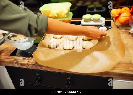 Eine verkürzte Frau knete Kekse oder Kuchen auf Backpapier in der Nähe eines schwarzen fernsehbildschirms in der Küche. Kulinarische Meisterklasse Stockfoto