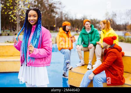 Multiethnische Gruppe junger, glücklicher Freunde, die sich im Winter im Freien treffen, Winterjacken tragen und eine lustige, modische schwarze Frau im Vordergrund haben - Mu Stockfoto