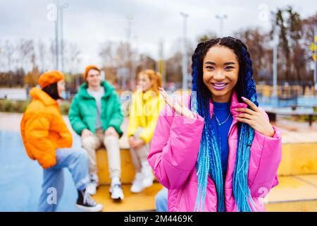 Multiethnische Gruppe junger, glücklicher Freunde, die sich im Winter im Freien treffen, Winterjacken tragen und eine lustige, modische schwarze Frau im Vordergrund haben - Mu Stockfoto