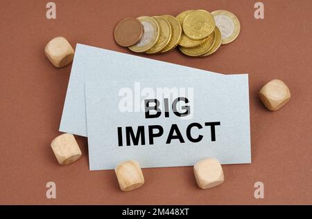 Geschäfts- und Finanzkonzept. Auf einer braunen Oberfläche befinden sich Münzen, Würfel und eine Visitenkarte mit der Aufschrift „Big Impact“