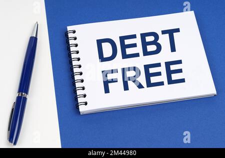 Geschäfts- und Finanzkonzept. Auf einer blau-weißen Oberfläche liegen ein Stift und ein Notizbuch mit der Aufschrift "Debt Free" Stockfoto