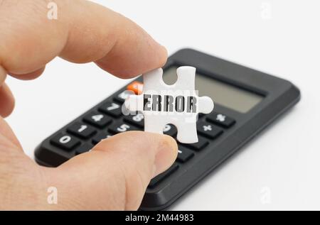 Wirtschafts- und Finanzkonzept. Ein Mann hält in seinen Händen ein Puzzle mit der Inschrift "Fehler". Im Hintergrund befindet sich ein Taschenrechner. Stockfoto
