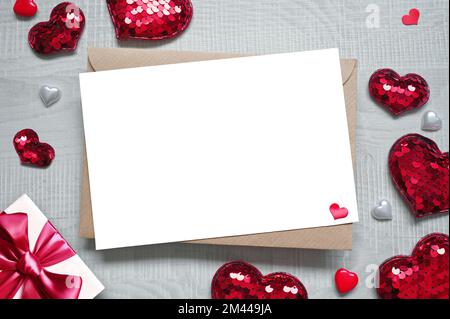 Leere weiße Grußkarte mit braunem Umschlag und Herzen auf Marmortisch. Modellkonzept Valentinstag Stockfoto