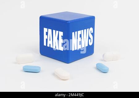 Medizin und Gesundheitskonzept. Auf einer weißen Oberfläche sind Pillen und ein blauer Würfel, auf dem "FAKE NEWS" steht Stockfoto