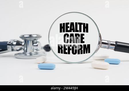 Medizin und Gesundheitskonzept. Auf einer weißen Oberfläche liegen Pillen, ein Stethoskop und eine Lupe mit der Inschrift - GESUNDHEITSREFORM Stockfoto