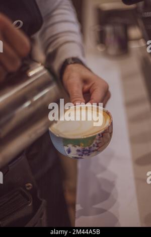 Nahaufnahme von männlichen Händen, die Milch eingießen und frischen Cappuccino zubereiten, Kaffeekünstler und Zubereitungskonzept, Morgenkaffee. Stockfoto