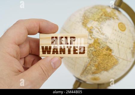 Globalisierungskonzept. Ein Mann hält in der Hand einen Holzteller, auf dem es steht - HILFE GESUCHT. Im Hintergrund ist ein Globus. Stockfoto