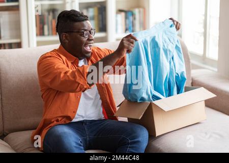 Aufgeregter, fetter afrikanischer Kunde, der die Lieferung überprüft, gutes Paket Stockfoto