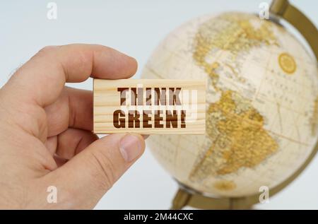 Globalisierungskonzept. Ein Mann hält in seiner Hand eine Holzplatte, auf der es steht - Think Green. Im Hintergrund ist ein Globus. Stockfoto