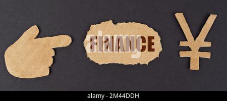 Wirtschafts- und Finanzkonzept. Auf einer schwarzen Oberfläche, einer Handfigur, einem Yen-Symbol und einem zerrissenen Karton mit der Inschrift "FINANZEN" Stockfoto