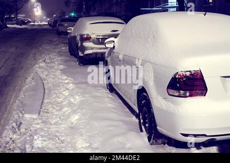 Autos mit Schnee bedeckt auf einer Stadtstraße bei Nacht Stockfoto