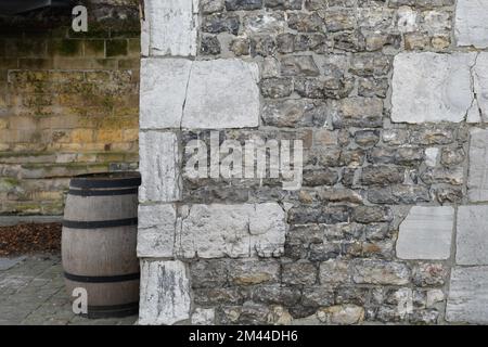 Ein Bruchteil eines alten Innenhofs, eine Steinmauer und ein altes großes Fass für Wein. Kreativer Hintergrund Stockfoto