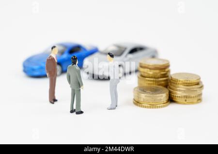 Autoverkauf, Autoverkauf, Deal. Auf der weißen Oberfläche befinden sich Autos, Münzen und Miniaturfiguren von Menschen. Einen Deal besprechen Stockfoto