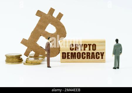 Kryptowährung und Geschäftskonzept. Auf der weißen Oberfläche der Münze befindet sich das Bitcoin-Symbol, Miniaturfiguren von Geschäftsleuten und eine Holzplatte mit der Stockfoto