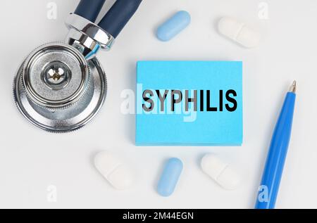 Medizin und Gesundheitskonzept. Auf einer weißen Oberfläche liegen Pillen, ein Stethoskop und Aufkleber mit der Inschrift - Syphilis Stockfoto