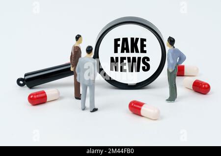 Medizinisches Konzept. Auf einer weißen Oberfläche sind Pillen, Miniaturfiguren von Menschen und eine Lupe mit der Inschrift "FAKE NEWS" Stockfoto