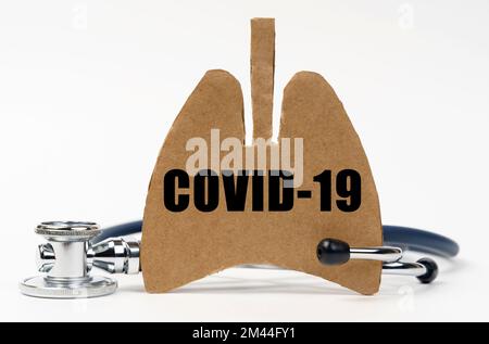 Medizinisches Konzept. Auf einer weißen Oberfläche befinden sich ein Stethoskop und eine Pappfigur einer Lunge mit der Inschrift - COVID-19 Stockfoto