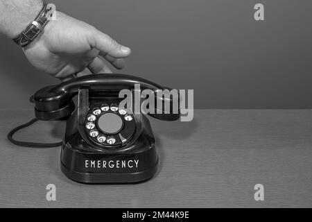 Notfall. Die Hand geht ans Telefon. Altes Telefon auf einem Holztisch, schwarz-weiß Stockfoto