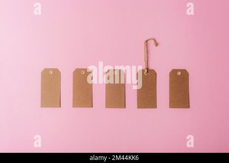 Braune Kraftpapieretiketten auf pinkfarbenem Hintergrund. Minimales flaches Verlegen. Draufsicht, Modell. Stockfoto