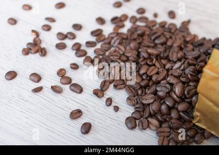 Kaffeebohnen aus der Verpackung sind mit Textur auf dem Tisch verstreut. Diagonal Stockfoto