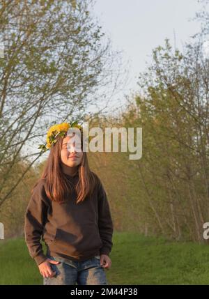 Porträt eines Teenagers bei Sonnenuntergang im Wald mit einem Löwenzahn. Geschlossene Augen Stockfoto