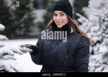 Eine elegante Frau kauft einen Weihnachtsbaum. Eine Frau in einem schwarzen Strickpullover. Eine schöne Frau wählt Tannenbaum Stockfoto