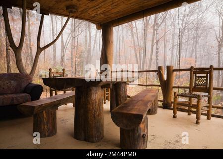 Esstisch aus gebeiztem und lackiertem Holz und Bänke im Sonnenzimmer, geschützt mit Netzen an rustikaler Blockhütte. Stockfoto