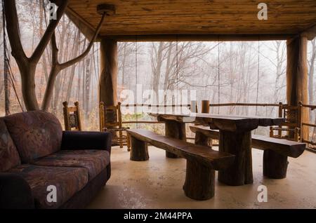 Esstisch aus gebeiztem und lackiertem Holz und Bänke im Sonnenzimmer, geschützt mit Netzen an rustikaler Blockhütte. Stockfoto