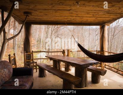 Esstisch aus gebeiztem und lackiertem Holz und Bänke im Sonnenzimmer, geschützt mit Netzen an rustikaler Blockhütte. Stockfoto