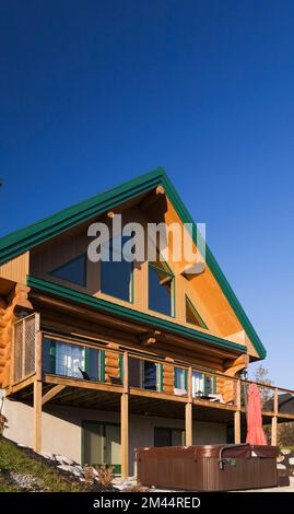 Rückansicht eines zweistöckigen Blockhauses im A-Rahmen-Stil mit Panoramafenstern, Balkon und grüner Verkleidung im Herbst. Stockfoto