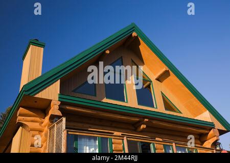 Rückansicht eines zweistöckigen Blockhauses im A-Rahmen-Stil mit Panoramafenstern und grüner Verkleidung im Herbst. Stockfoto