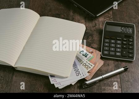 Buchfragment eines Kontogeräts mit Euro-Banknoten und einem Füllfederhalter auf einem Holztisch. Stockfoto