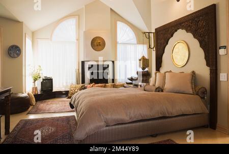 Queen-Size-Bett mit Holzkopfteil im marokkanischen Stil dekoriertes Hauptschlafzimmer in luxuriösem zeitgenössischem Haus. Stockfoto