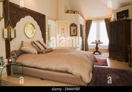 Queen-Size-Bett mit Holzkopfteil im marokkanischen Stil dekoriertes Hauptschlafzimmer in luxuriösem zeitgenössischem Haus. Stockfoto