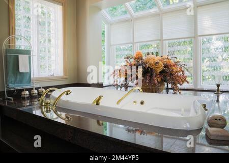 Weiße Jacuzzi-Badewanne mit Messingarmaturen in Granitbasis im marokkanischen Stil dekoriert Hauptbadezimmer im zeitgenössischen Haus. Stockfoto