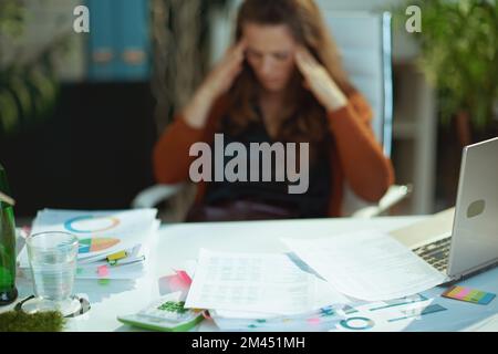 Nahaufnahme auf Tisch mit Dokumenten und gestresster Frau im Hintergrund im grünen Büro. Stockfoto