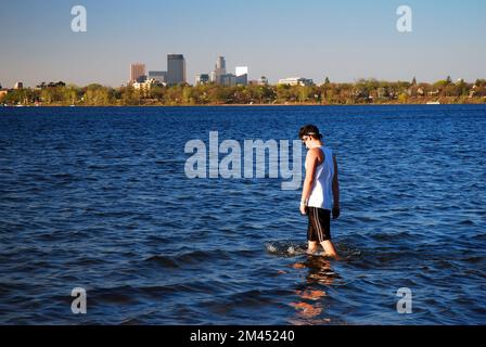 Ein erwachsener Mann waten am Lake Calhoun, mit der Skyline von Minneapolis im Hintergrund, an einem sonnigen Sommerferientag Stockfoto