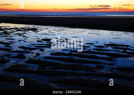 Wasserrutschen im Sandstrand reflektieren den Sonnenaufgang entlang der Küste Stockfoto