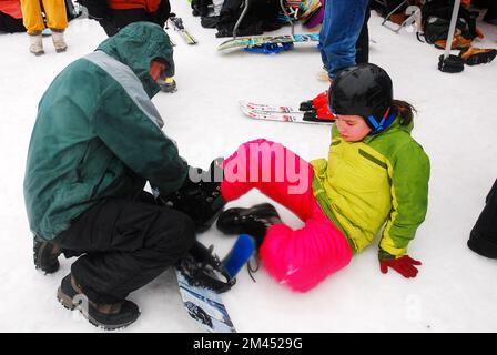 Ein junges Mädchen wird für ein Snowboard gerüstet, bevor es auf die Winterberge mit schneebedeckten Hängen des Berges geht Stockfoto