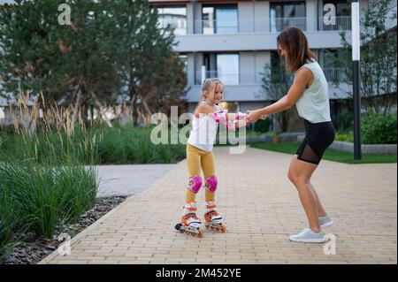 Mutter hilft Tochter, Rollschuh zu lernen. Stockfoto